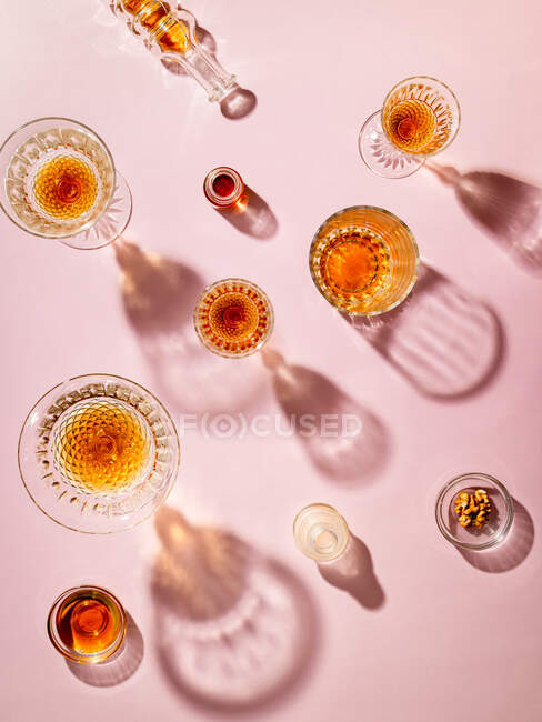 Vista superior de taças de vidro cheias de uísque lançando sombras criativas em fundo rosa em estúdio — Fotografia de Stock