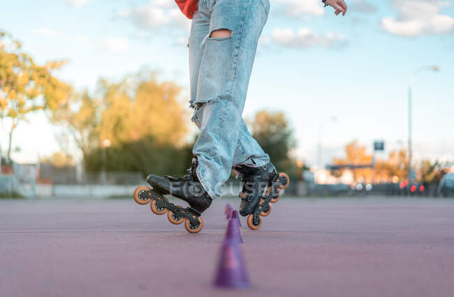 Crop unrecognizable person wearing blue jeans and black roller blades training with cones in skate park — Stock Photo