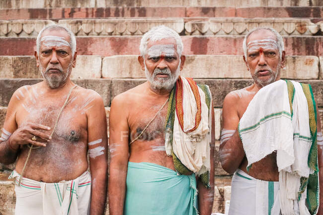INDIA, VARANASI - 27 DE NOVIEMBRE DE 2015: Hombres sin camisa de mediana edad con el pelo gris y con ropa casual de pie cerca del edificio de mala calidad y mirando a la cámara - foto de stock