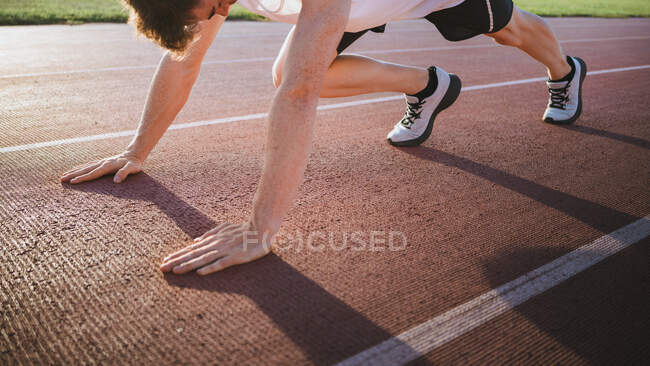 Кукурудзяний спортсмен у кросівках, що стоять на стартовій позиції перед тренуванням на треку на сонячному світлі — стокове фото