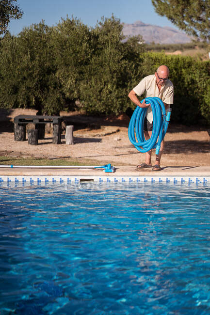 Повне тіло старшого чоловіка в окулярах стоїть з гумовим шлангом для басейну — стокове фото