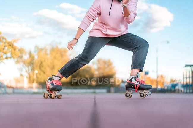 Cropped unrecognizable active young woman skater wearing pink hoodie and black jeans with roller skates practicing skills in skate park — Stock Photo