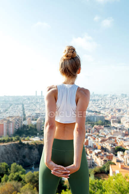Back view of unrecognizable mindful young fit female athlete in sportswear stretching arms during workout in sunny city — Stock Photo