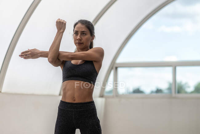 Young ethnic female athlete in active wear with raised arms looking forward during stretching training in daytime — Stock Photo