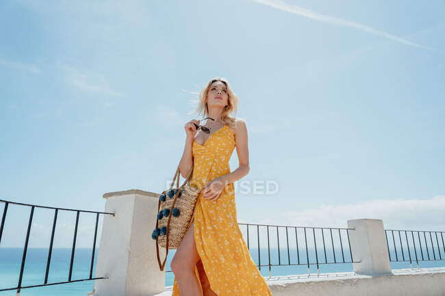 Voyageuse en robe debout près de la clôture et admirant la vieille ville côtière pendant les vacances d'été — Photo de stock