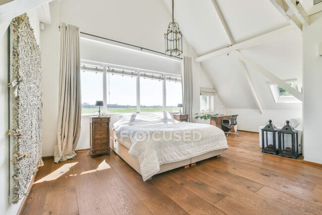 Cover on bed under vintage lamp hanging against window in modern bedroom on sunny day — Stock Photo