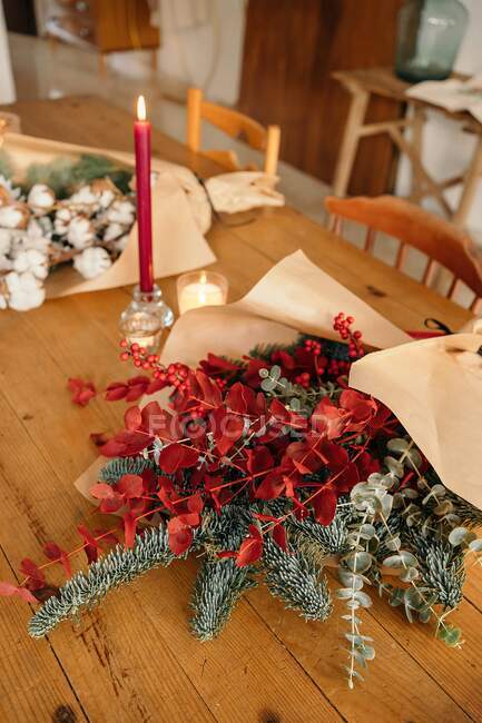 Зверху святковий стильний декоративний різдвяний букет з гілочками евкаліпту і яскраво-червоними гілками з ягодами на дерев'яному столі з свічками в кімнаті. — стокове фото