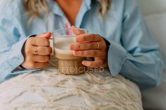 Colheita fêmea adulta com cabelo ondulado bebendo café saboroso enquanto olha para a frente em casa — Fotografia de Stock