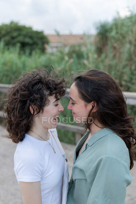 Side view of trendy young woman with homosexual beloved looking at each other on bridge — Stock Photo