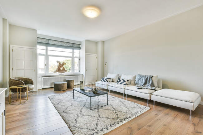 Weiche Couch mit Kissen in der Nähe des Tisches auf Teppich im geräumigen hellen Wohnzimmer mit Sessel in der Nähe des Fensters — Stockfoto