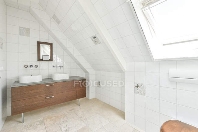 Interior de baño contemporáneo con varillas de incienso en estante contra lavabos entre armarios y espejos en casa de luz - foto de stock