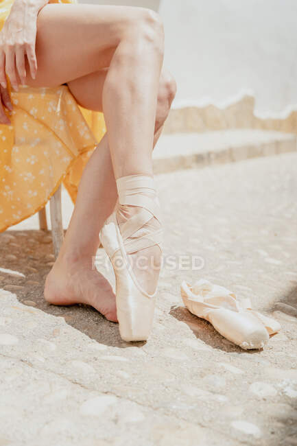 Crop unrecognizable ballerina wearing long dress and pointe shoe sitting on chair on street — Stock Photo