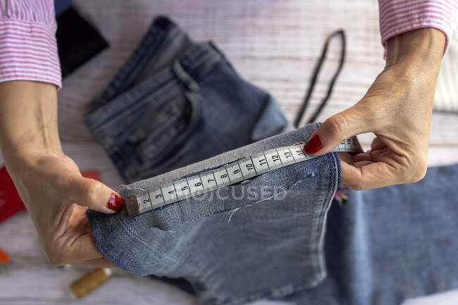From above of crop anonymous female dressmaker using measuring tape while sewing jeans in atelier in daytime — Stock Photo