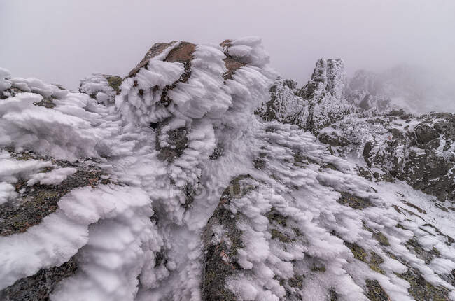 Nieve sobre formación rocosa de cordillera situada en el Parque Nacional Sierra de Guadarrama en clima nebuloso - foto de stock