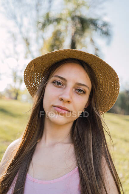 Charming female teen with long hair looking at camera in sunny park on blurred background — Stock Photo