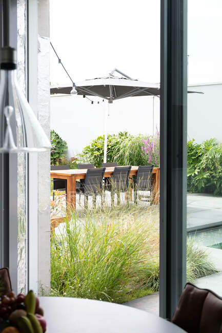 Інтер'єр кімнати з вікном з видом на терасу з зеленими рослинами і дерев'яним столом вдень — стокове фото