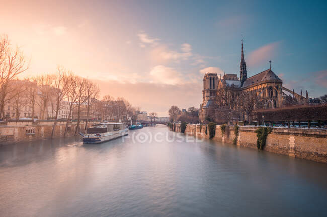 Barco turístico flotando en el agua ondulada del río Sena pasando por la catedral católica medieval de Notre Dame de Paris al atardecer - foto de stock