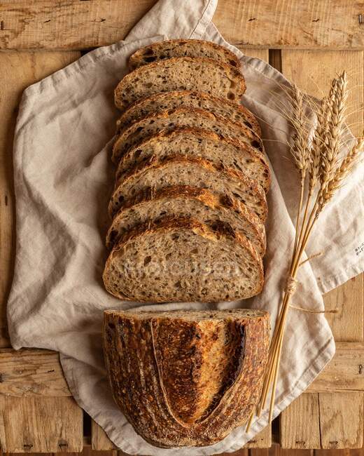 Top view of fresh cereal bread pieces with wheat spikes on creased textile on wooden surface — Stock Photo