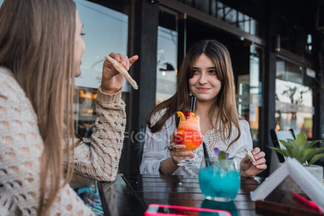 Crop content best female friends with tasty beverages and snacks speaking while looking at each other in street cafeteria — Stock Photo