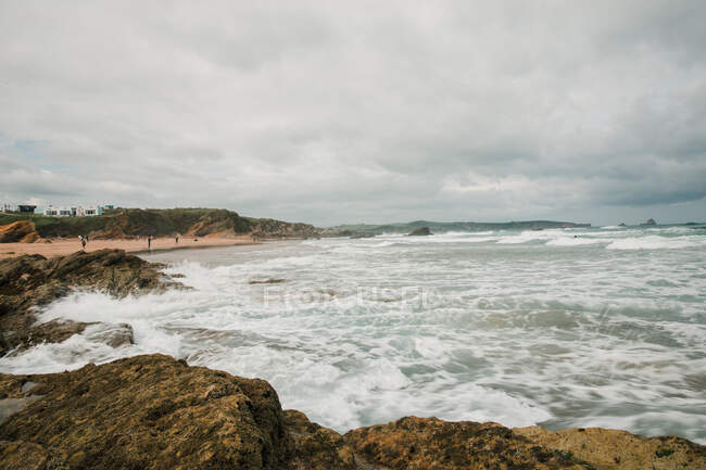 Vue panoramique de la mer ondulée avec des flux d'eau mousseuse contre la plage rugueuse avec montagne en Cantabrie Espagne — Photo de stock