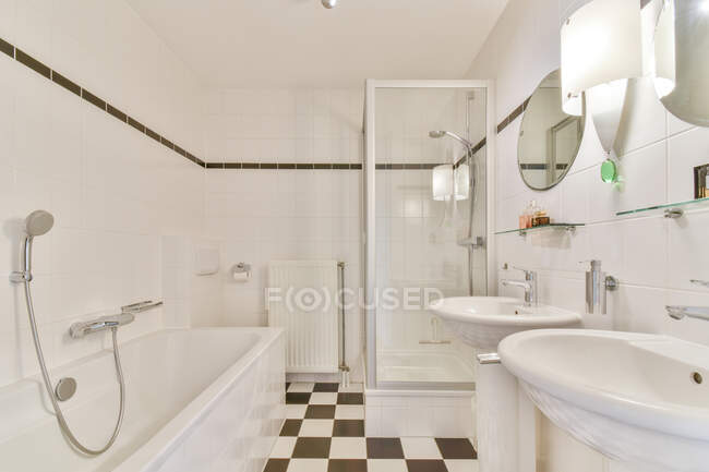 Kreative Gestaltung des Badezimmers mit Lampe zwischen Waschtischen gegen rechteckige Badewanne auf Fliesenboden im Haus — Stockfoto