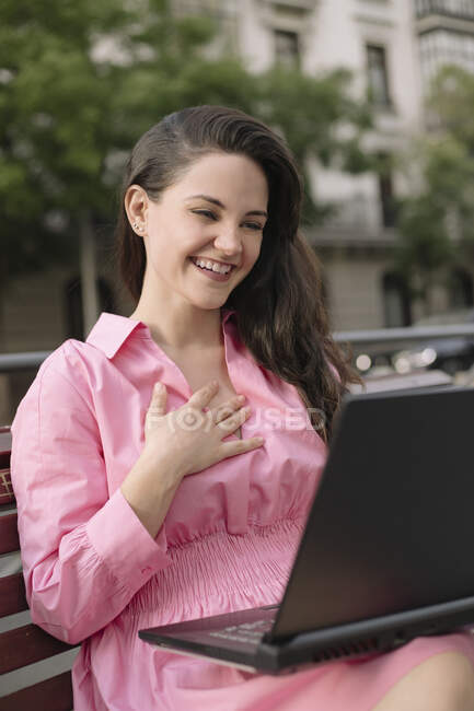 Joyeux jeune femme d'affaires en robe assis sur le banc de travail sur netbook sur la rue de la ville — Photo de stock