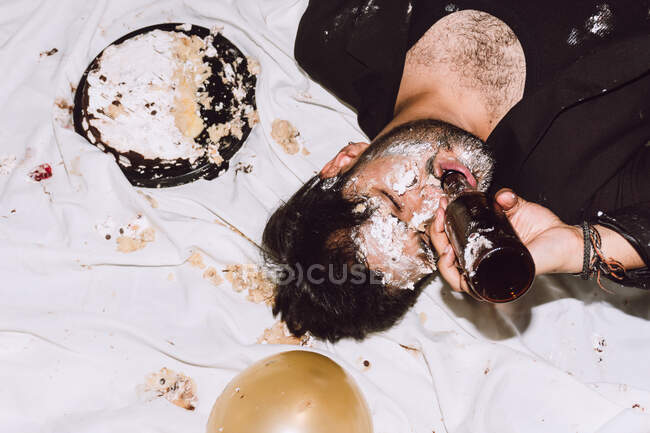 Сверху пьяный мужчина с закрытыми глазами и лицом, покрытым разбитым тортом во время празднования дня рождения — стоковое фото