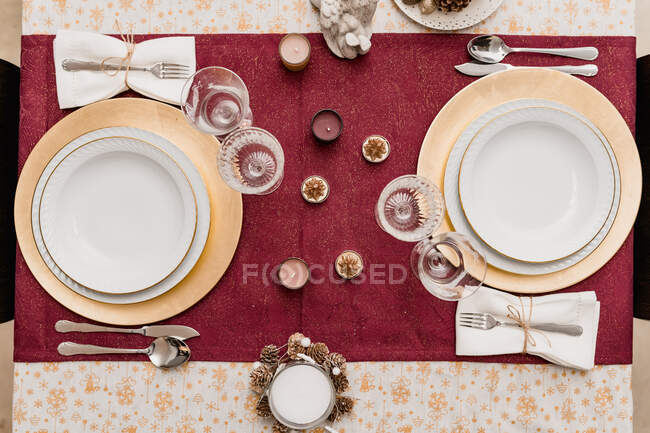 Top view of table setting with glasses and cutlery near plates decorated with candles and cones for Christmas celebration — Stock Photo
