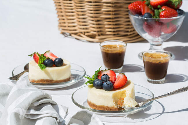 Tasty sweet cheesecakes with blueberries and strawberries served on glass table near cups of coffee — Stock Photo
