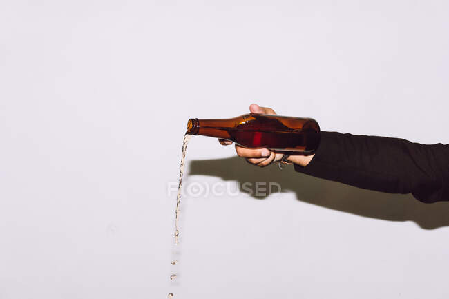 Crop anonymous male pouring beer from transparent glass bottle at party against white background — Stock Photo