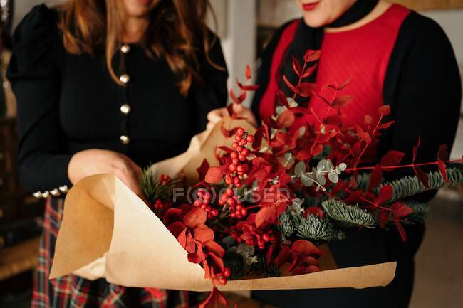 Cortado amigos do sexo feminino irreconhecíveis em pé à mesa com velas e fazendo buquês de Natal criativo para a celebração do feriado — Fotografia de Stock