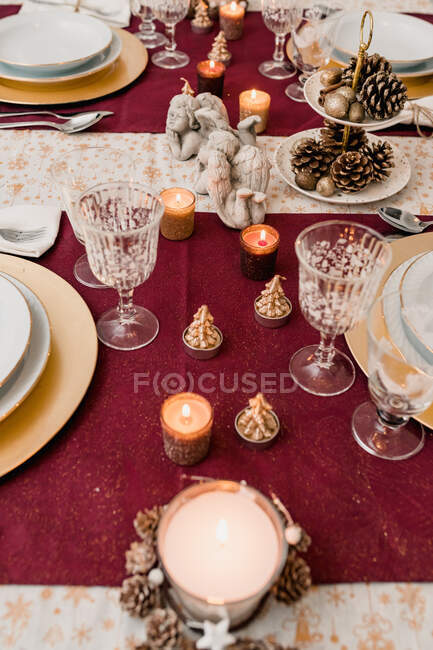 Desde arriba de mesa de banquete servido con vajilla y vasos y decorado con velas y conos encendidos para la cena de Navidad - foto de stock