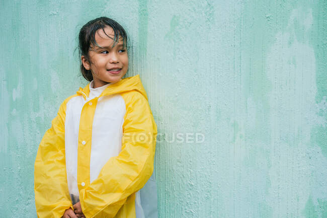 Charmantes ethnisches Kind in Slicker, das auf pastellfarbenem Hintergrund wegschaut — Stockfoto