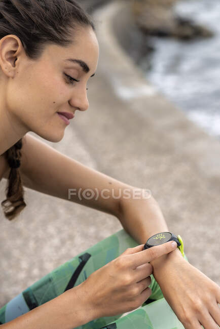 Corredor femenino comprobando el pulso en el moderno brazalete de fitness portátil durante el entrenamiento en la ciudad - foto de stock