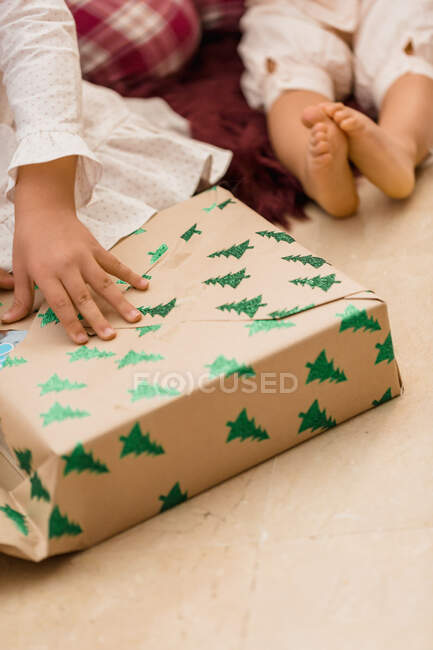 Анонимный урожай ребенка открытие подарка коробка с рисунком елки на полу во время новогоднего праздника в доме — стоковое фото