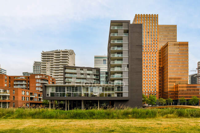 Высокие современные здания экстерьеров против тротуара с деревьями и рекой под облачным небом в Амстердаме Голландия — стоковое фото