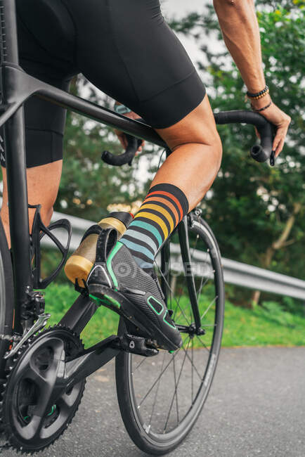 Vue arrière de l'athlète masculin méconnaissable en chaussures de cyclisme et chaussettes rayées à vélo pendant l'entraînement sur route — Photo de stock