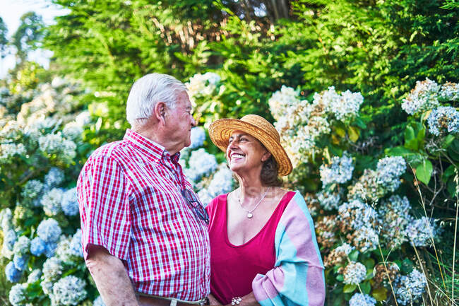Gentile coppia anziana accarezzando guardarsi con tenerezza mentre in piedi vicino a cespugli in fiore in natura — Foto stock