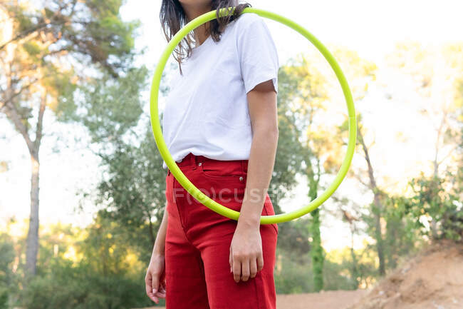 Обрізати невпізнавану жінку-підлітка в червоних джинсах, тримаючи обруч, маючи вільний час у парку — стокове фото