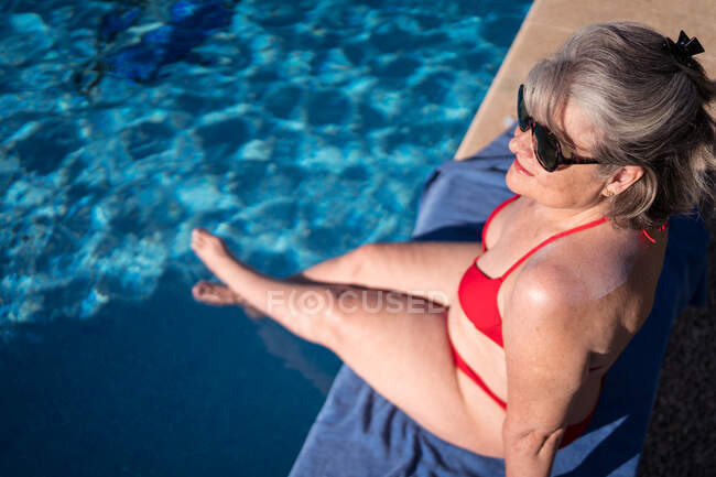 Зверху жінка-мандрівник сидить на краю басейну з схрещеними ногами у чистій блакитній воді — стокове фото