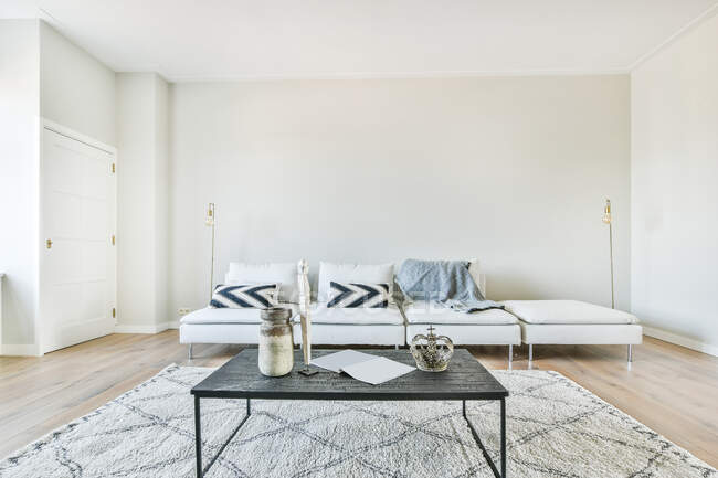 Morbido divano con cuscini vicino al tavolo posizionato sul tappeto in ampio soggiorno luminoso con poltrona — Foto stock