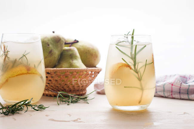 Cóctel de pera fría en vasos con romero y cubitos de hielo colocados sobre la mesa con frutas frescas - foto de stock