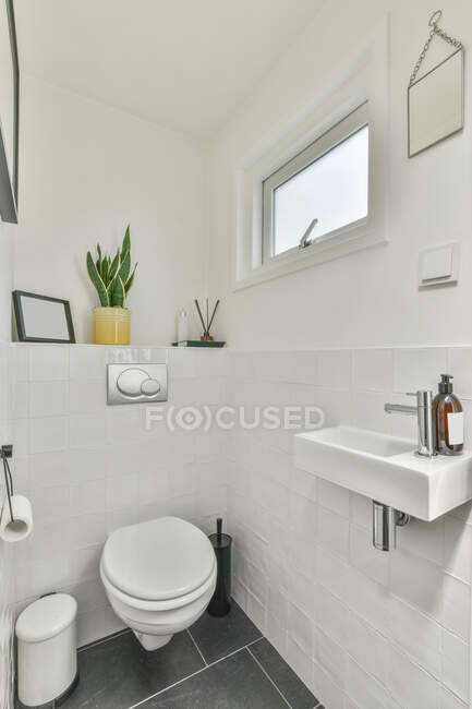 Limpia lavabo pequeño e inodoro en baño ligero paredes de baldosas blancas en apartamento moderno - foto de stock