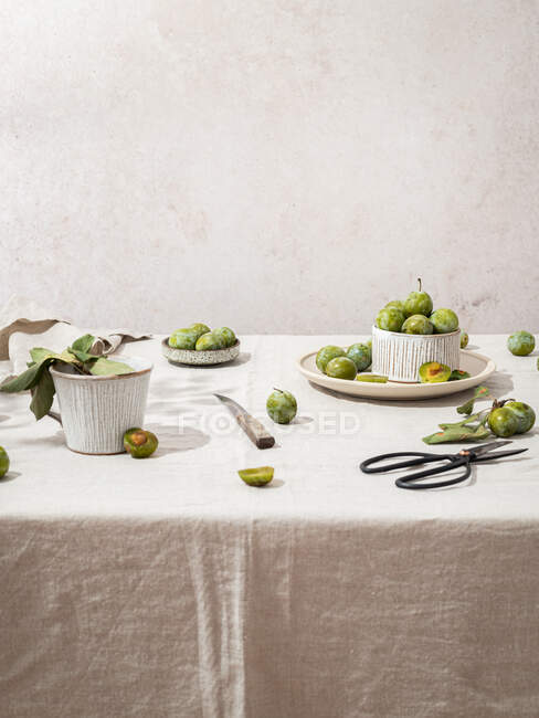 Ainda composição de vida de ameixas frescas verdes arranjadas com utensílios de mesa na mesa coberta com toalha de mesa — Fotografia de Stock
