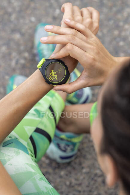 Сверху урожая анонимная бегунья проверяет пульс на современном носимом фитнес-браслете во время тренировки в городе — стоковое фото
