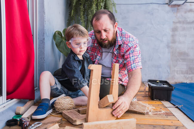 Focado pai barbudo em camisa quadriculada com menino trabalhando com blocos de madeira — Fotografia de Stock