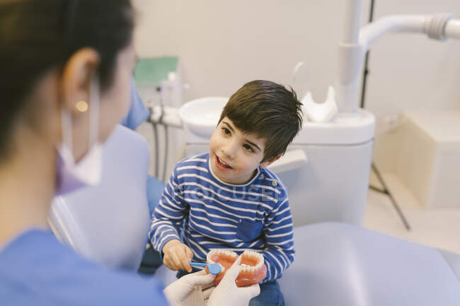 Lächelnde Kieferorthopädin lehrt Patientin mit Zahnbürste Zähne am Kiefermodell in Zahnklinik zu putzen — Stockfoto