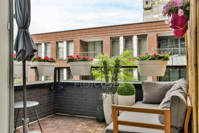 Balcone di casa con cuscini su panchina di tessuto contro tavolo e fiori fiorenti in pentole sotto cielo nuvoloso — Foto stock