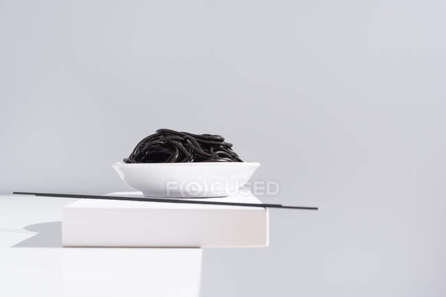Du dessus du bol en céramique avec de délicieux spaghettis à l'encre de calmar noir avec des baguettes sur fond blanc — Photo de stock