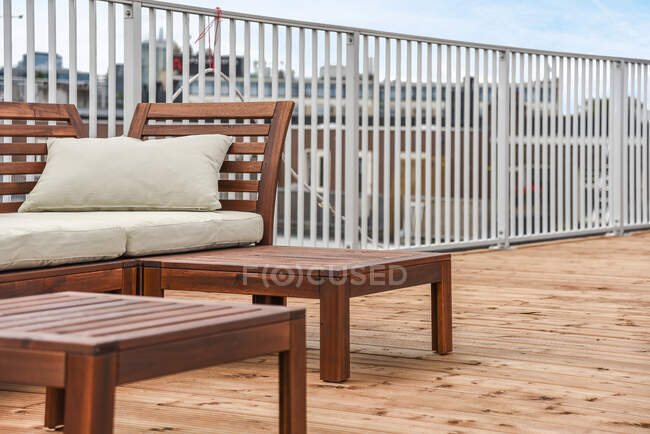 Диван расположен возле деревянного стола на огороженном балконе жилого пригорода в дневное время — стоковое фото